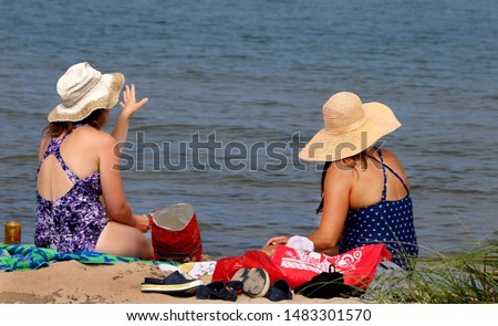 two women wearing hats at the beach watching their children