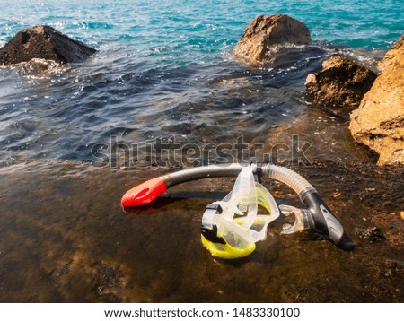 Mask and snorkel on the weed covered stone pier against splashing sea waves at the background