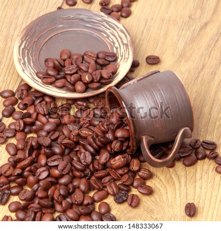 Dark brown coffee beans in small ceramic coffee cup over light brown wooden background