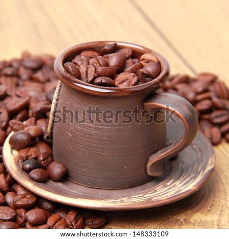 Delicious dark brown coffee beans in ceramic coffee cup over light brown wooden background