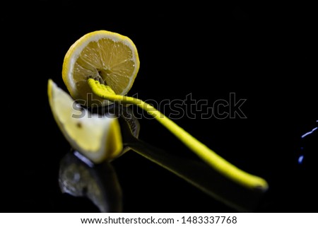 A cut yellow lemon, on a bright black background and with a yellow fork stuck in the lemon. everything is reflected in the base,