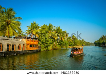 A tourist boat passes through a traditional Kerala houseboat on the backwater of Vembanad Lake Royalty-Free Stock Photo #1483337930