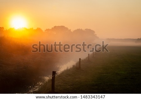 Beautiful misty morning in the Netherlands with a orange rising sun and a small ditch in farmers land, picture taken in the province Overijssel 