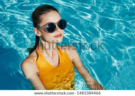  woman in a yellow bathing suit and glasses stands in the pool transparent water sun summer                              
