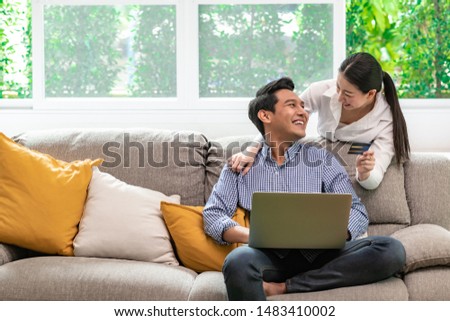 Couple online shopping at home in living room sofa. Asian man and woman, happy smile. Royalty-Free Stock Photo #1483410002