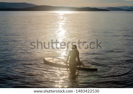 Silhouette of a teenage girl sitting on a paddle board on Flathead Lake in Montana