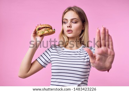woman in a striped T-shirt holds a hamburger in her hands diet ration pink background
