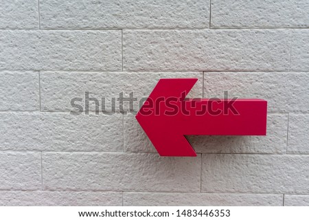 Pink arrow sign  hanging against white bricks wall for direction.