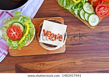 On a dark wooden surface is an open homemade burger with a slice of cheese on top of the vegetarian meatball, on which the word veggie was written with ketchup - a concept for vegetarian nutrition