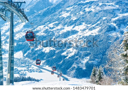 Red Cable cars in Zillertal Arena ski resort in Tyrol in Mayrhofen, Austria in winter Alps. Chair lifts in Alpine mountains with white snow and blue sky. Downhill fun at Austrian snowy slopes.