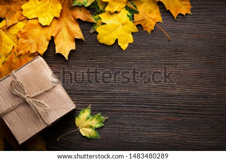 cardboard box tied with string on a bow on a wooden background in autumn leaves, holiday gift on Thanksgiving Halloween. top view f. copy space