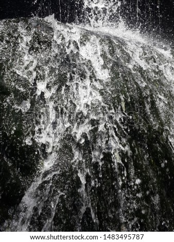 Close up view of water flowing over stone on a day, pure white water splashes on a black rock when running