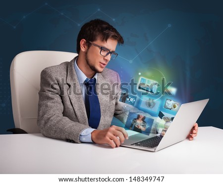 Attractive young man sitting at desk and watching his photo gallery on laptop