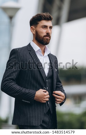 Confident businessman. Confident young man in full suit adjusting his sleeve and looking away while standing outdoors with cityscape in the background