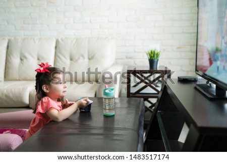 Little kid having breakfast while watching TV in living room at home