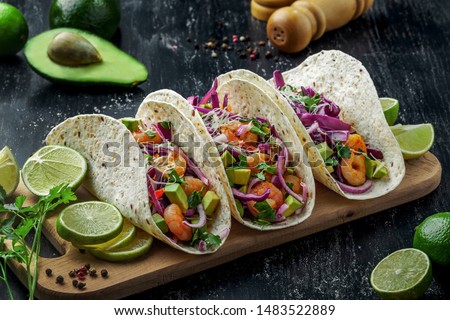 Delicious tacos with shrimps, avocado, onion and lime on a wooden board. Classic Tex-Mex cuisine meal.