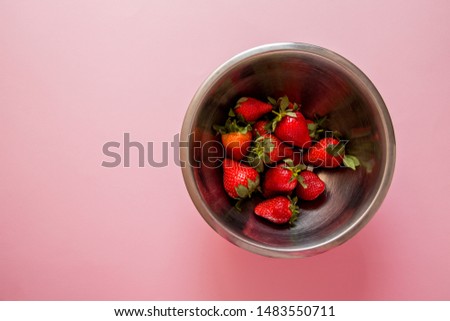 Juicy strawberry in metal bowl on pink background. View from the top.