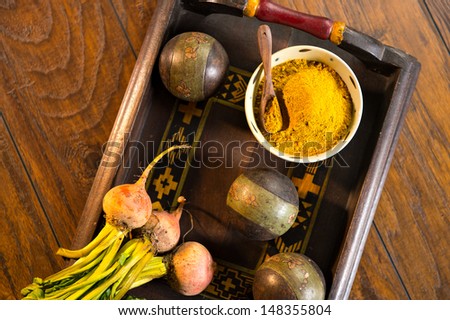 Ceramic bowl filled with yellow curry powder with a wood spoon on a decorative wooden tray. The tray is shot on a wood surface.  Beet roots are also pictured.