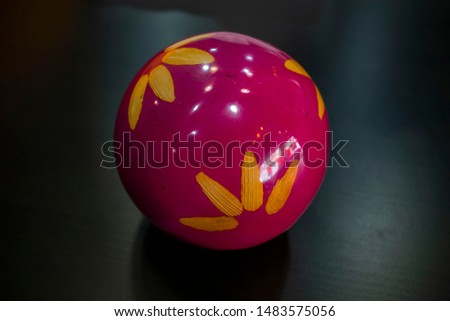 Pink ball with light reflections, has some yellow flower petals and stands out with the black color of the background.