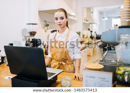 Caucasian attractive woman barista standing at the counter bar of a modern coffee shop.