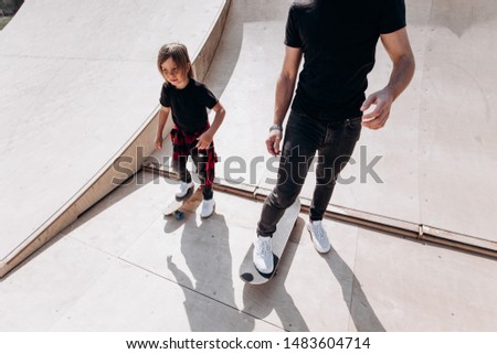 Happy father and his little son dressed in the casual clothes ride skateboards in a skate park with slides at the sunny day