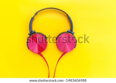 Red headphones on yellow background. Minimalist simple photo of earphones with copy space. Red dj headphones with cable isolated on colorful backdrop, flat lay top view. Music concept