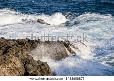 Powerful waves crashing into rocks in a mediterranean sea, blue water with foam.