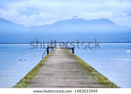 Wooden pier with stairs, relaxing jetty in a calm lake with cloudy weather and big blue mountains in the background.