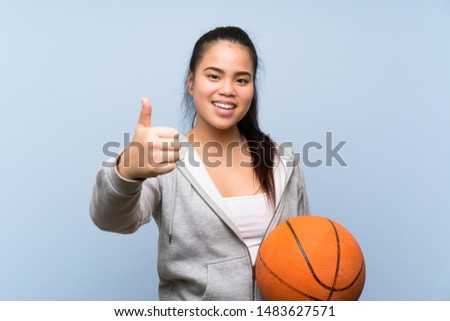 Young Asian girl playing basketball over isolated background with thumbs up because something good has happened
