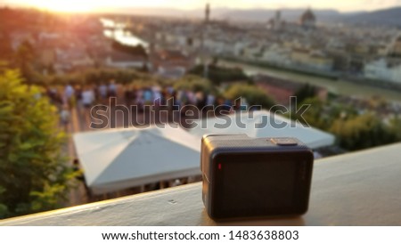 Black sport camara recording a time lapse of a sunset in Florence, Italy at the popular tourist spot, Piazzale Michelangelo.  Focus on camera, blurred backdrop and sun flare. 