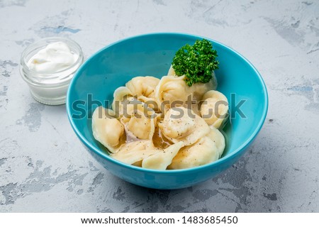 Dumplings with sour cream and herbs on grey concrete table