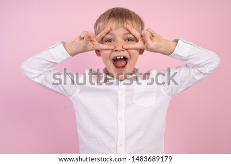 Close up photo of cheerful kid make victory signs laugh feel rejoice isolated over pink background.