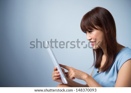 Portrait of Asian woman reading a tablet pc indoor wearing blue dress isolated on blue background. Asian female model.