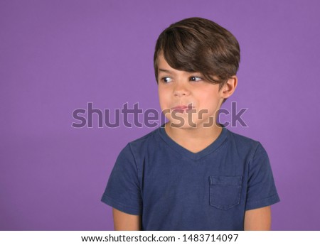 Funny little boy looking to side with silly  expression isolated on purple background Royalty-Free Stock Photo #1483714097