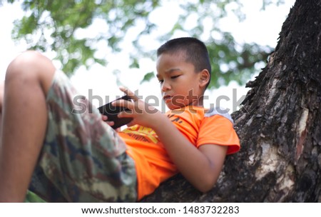 child with smartphone on big tree. be touching to screen, playing games or using application. nature and softlight background.