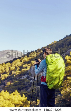 Man with trekking poles and backpack taking picture on a mountain trail