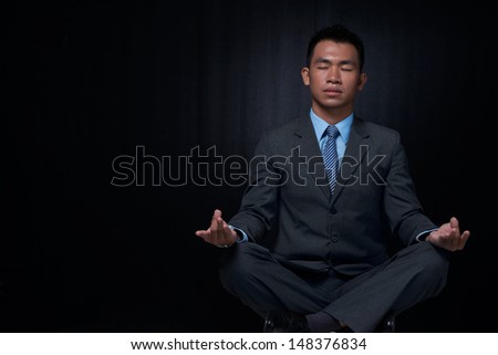 Copy-spaced image of a relaxed businessman resting in yoga position against a black background