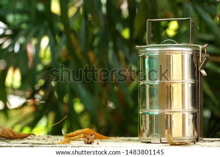 Antique aluminum stainless steel food carrier (Tiffin container or lunch box) 3 step on floor at the garden. Still life. Simple style. Copy space. Royalty-Free Stock Photo #1483801145