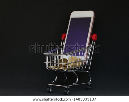 Online shopping concept. Smartphone with cart and coins and black background                          