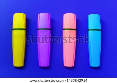 four neon markers for office and study of purple pink blue and yellow colors are arranged vertically and parallel to each other on a bright blue background. minimalism. flat lay