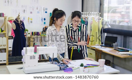 Designing new clothes. Beautiful young women dressmakers working on sketches and swatches while standing in modern workshop. ladies colleagues fashion designers discussing in cozy light studio.
