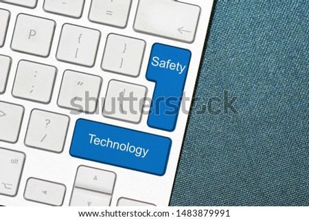 White computer keyboard and blue buttons with words Safety and Technology. Dark background. Close-up.