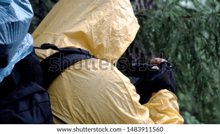 Traveler takes pictures in forest in cloudy weather. Stock footage. Hiker explores area and takes pictures of forest environment on camera in raincoat in cloudy weather