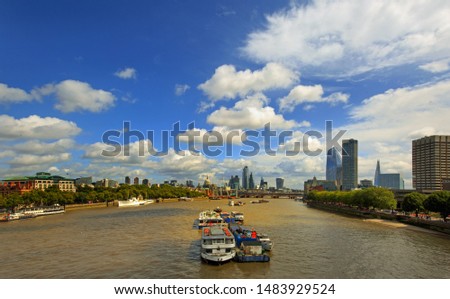 Scenic view of the River Thames with various iconic buildings and barges against a bright blue cloudscape sky