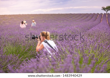 Beautiful woman taking picture outdoors with a DSLR camera. Young blonde woman, professional photographer, taking pictures of a beautiful nature surrounding her, warm sunny day in lavender field. 