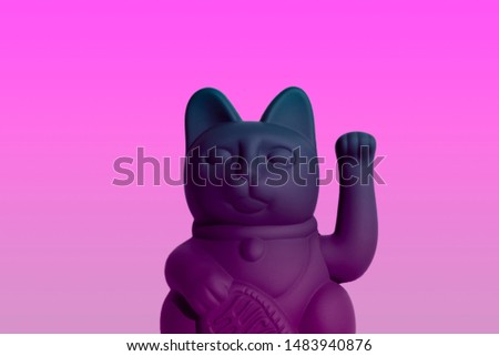 Manekineko with a coin. Good luck plastic matted cat on a pink background. The effect of degradation.