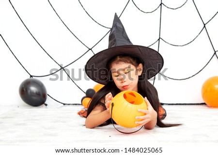 The concept of Halloween, funny face. Funny asian children girl in witch dress costume for Halloween decoration with pumpkins and holiday attributes. Children's party. 