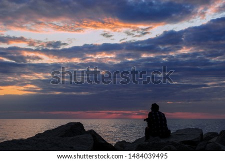 Colorful seascape with a silhouette of a one man sitting on the rock  under the cloudy dramatic sky during sunset.
