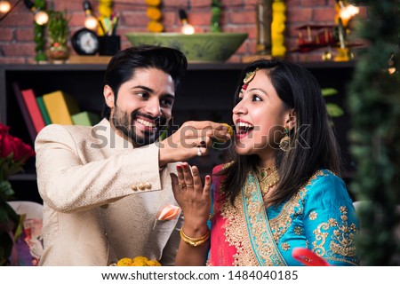 Indian smart couple eating sweet laddu on Diwali or anniversary, selective focus Royalty-Free Stock Photo #1484040185