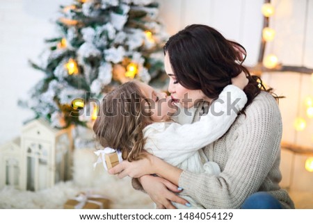 Beautiful happy mother with lher ittle daughter in knit sweater sitting on the background of Christmas interior hugging together and smiling 